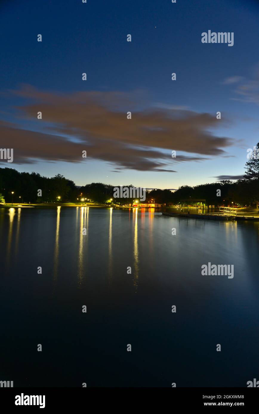 Vue verticale d'une longue exposition du lac Beaver, Mont-Royal, Montréal, QC, Canada à l'heure bleue au crépuscule, par une journée d'été nuageuse. Les lumières et l'arbre Banque D'Images