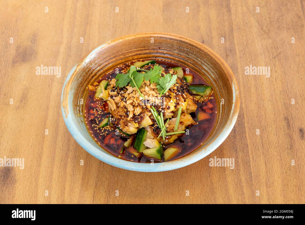 Ramen de poulet épicé avec morceaux de courgettes, arachides, persil et graines de sésame dans un bol en céramique Banque D'Images