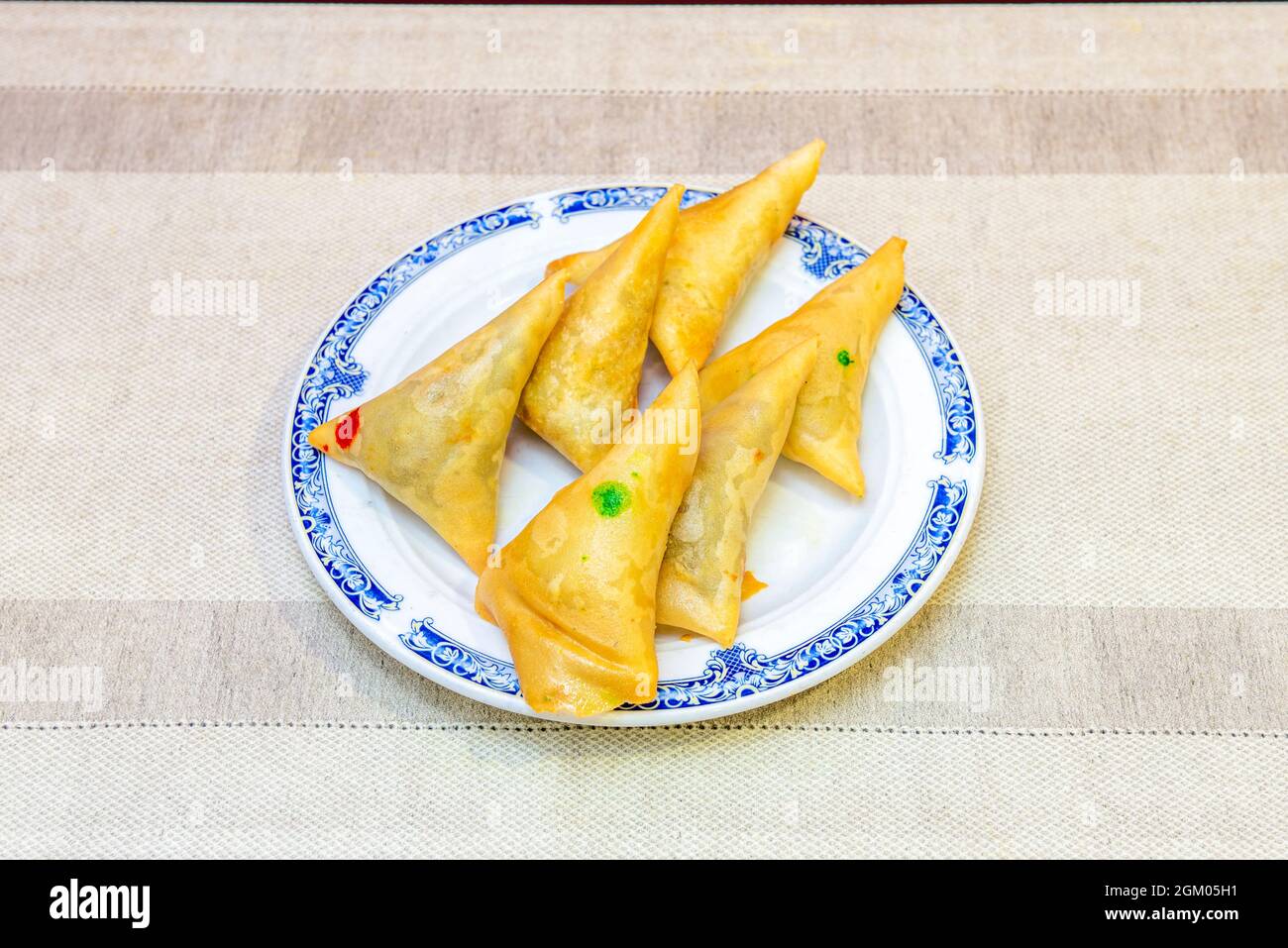 Les samosas farcies de viande et de légumes marqués pour les distinguer sur une assiette à bord bleu et sur une table beige dans un restaurant pakistanais Banque D'Images