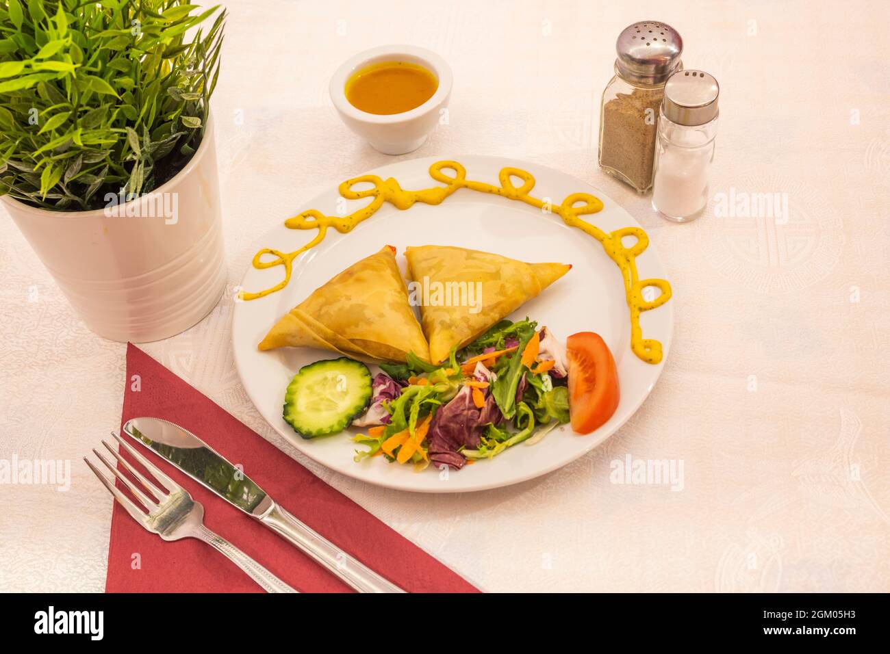 Samosas frites avec garniture de salade servies dans un restaurant pakistanais avec des serviettes en papier rouge. Banque D'Images