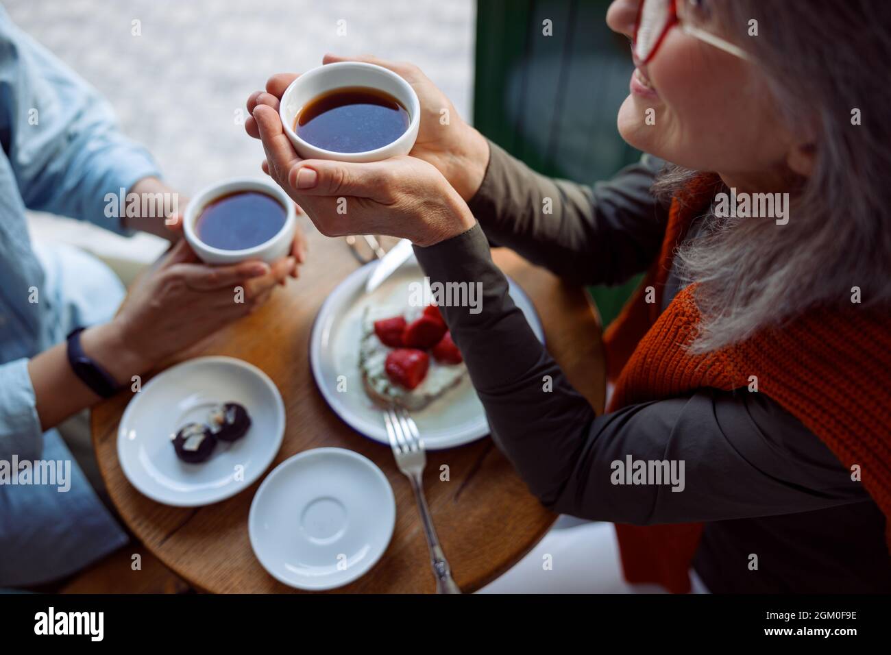 Une femme mûre souriante avec un ami tient des tasses de thé assis à une petite table dans le café Banque D'Images