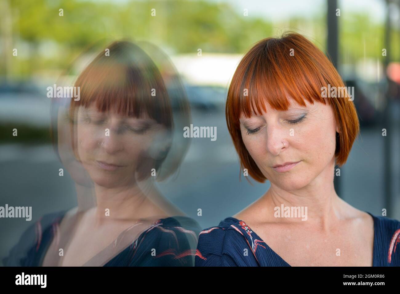 Femme abattue avec une expression triste et les yeux bagués debout contre une fenêtre de magasin dans la ville reflétée dans le verre dans une tête de gros plan Banque D'Images