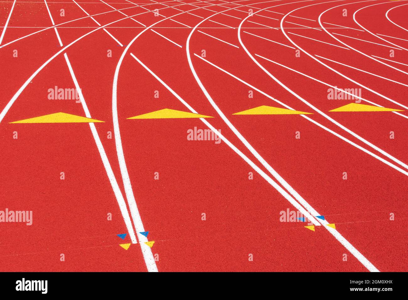Lignes blanches, triangles jaunes et marques de haies sur la courbe de la piste de course en caoutchouc toutes saisons. Banque D'Images