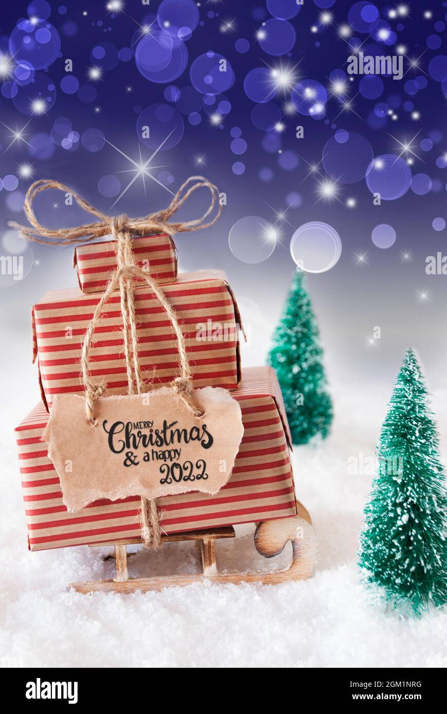 Traîneau avec cadeau de Noël et étiquette avec la calligraphie anglaise Joyeux Noël et Un heureux 2022. Neige avec sapin de Noël et fond violet étincelant Banque D'Images
