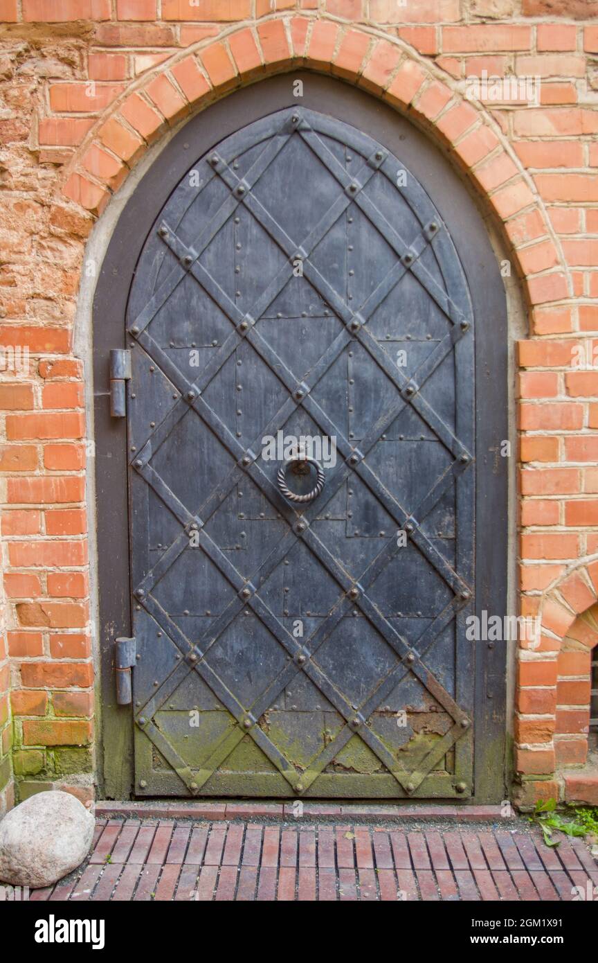 Ancienne façade de bâtiment avec porte en fer d'époque avec poignée circulaire dans le centre de la vieille ville en Lituanie. Porte de grunge en métal avec de la rouille et de la moisissure verte dans le mur de brique d'une église Banque D'Images