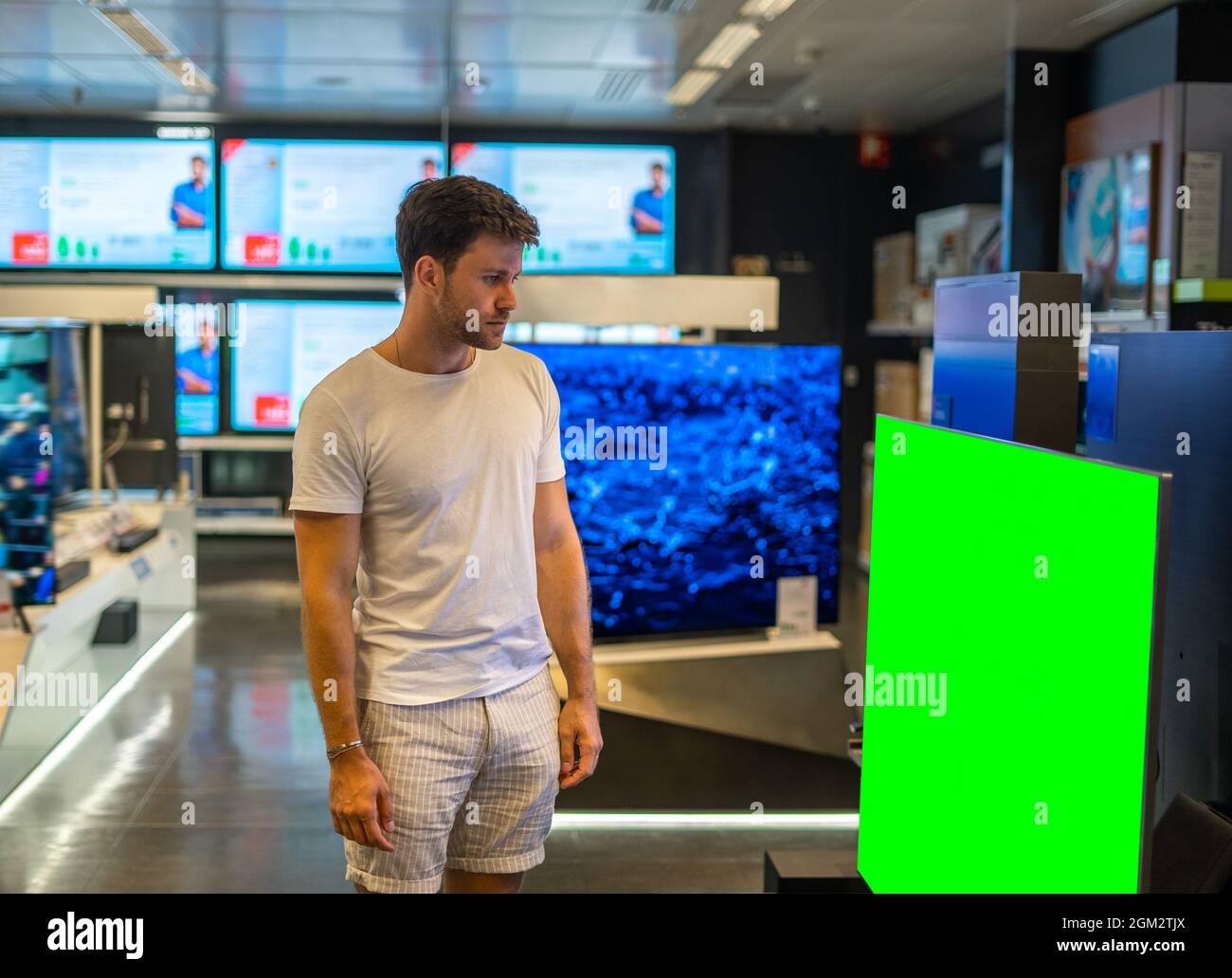 Jeune homme barbu se tenant devant un grand écran plat avec écran couleur verte lors d'une visite d'un magasin d'électronique moderne Banque D'Images