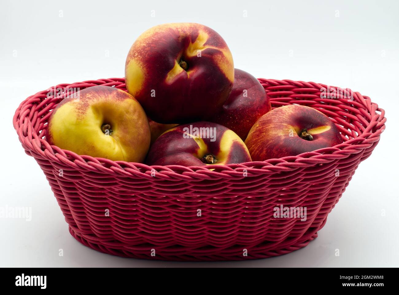Pêches mûres dans un panier rouge isolé sur fond blanc Banque D'Images