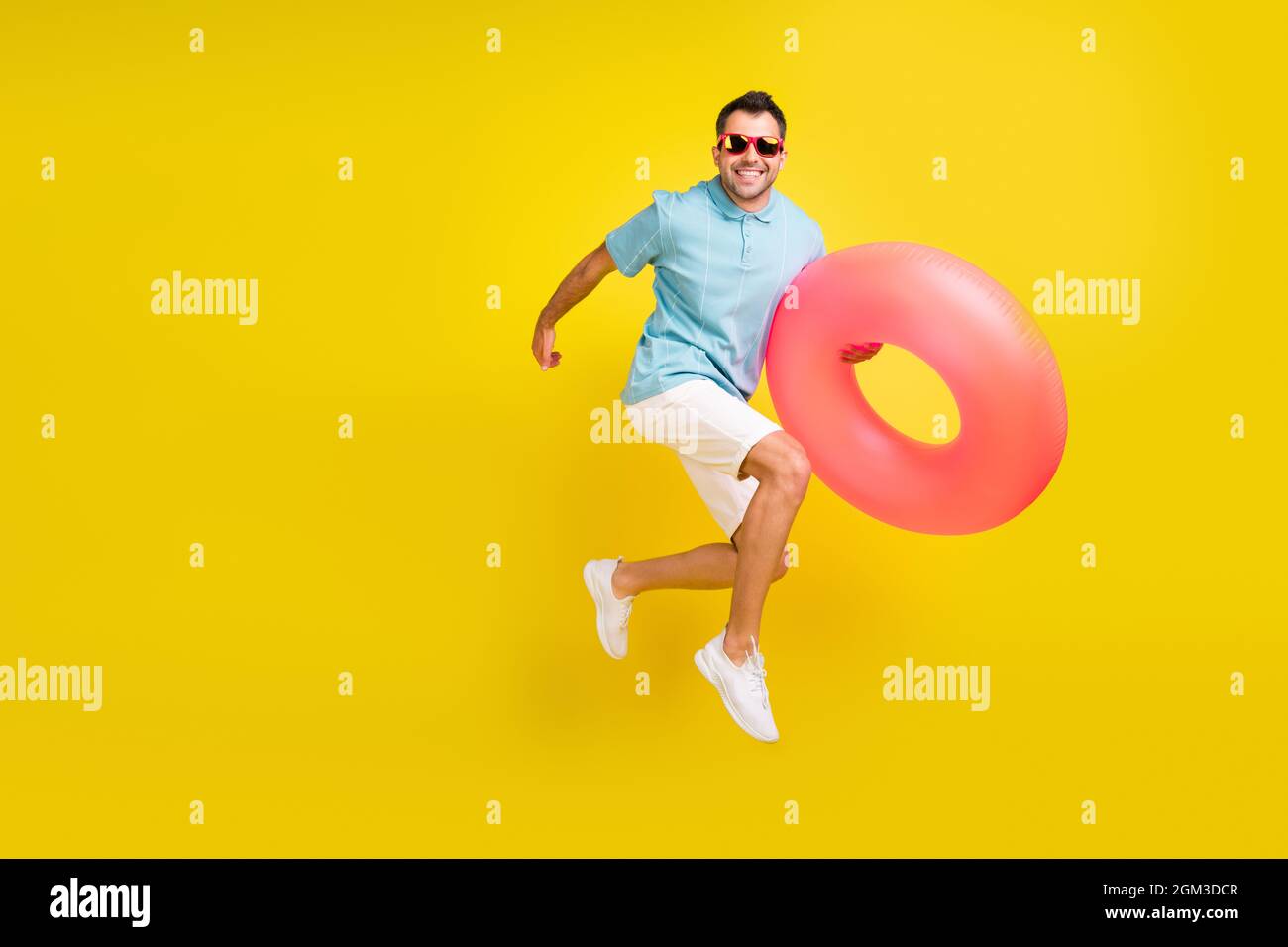 Photo de joli doux jeune gars habillé bleu t-shirt sombre oculaire courant jumping tenant anneau gonflable isolé couleur jaune fond Banque D'Images