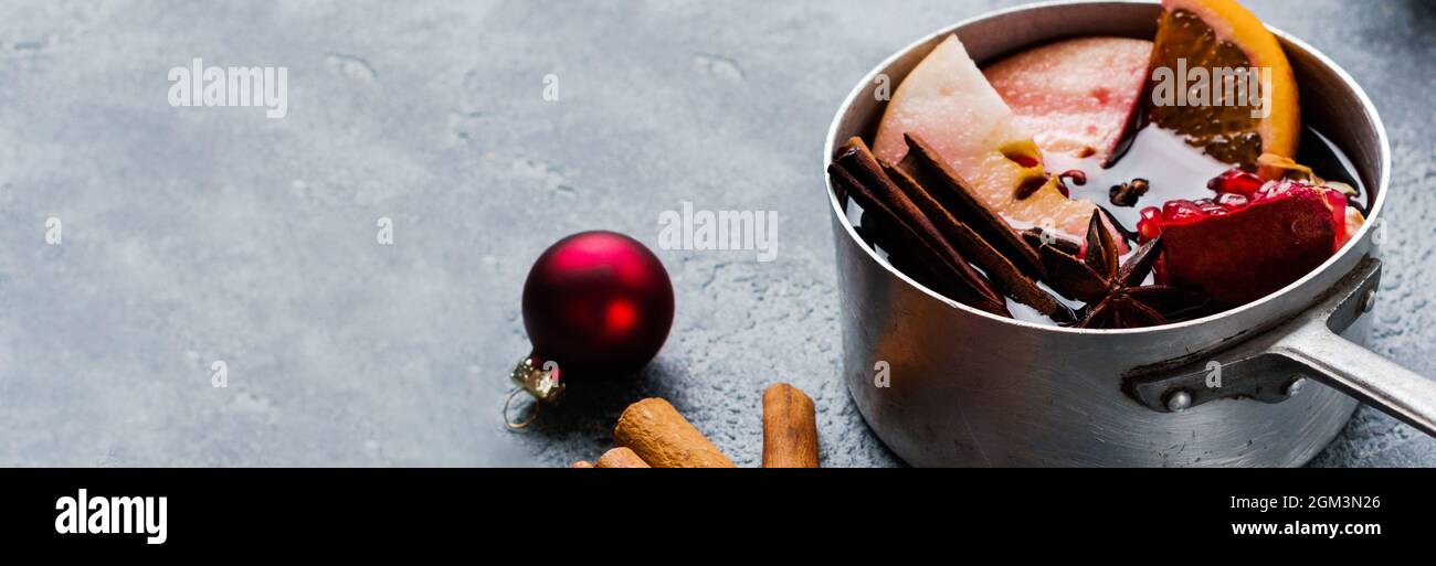 Boisson chaude au vin chaud avec agrumes, pomme, grenade et épices dans une casserole en aluminium avec jouets d'arbre de Noël vintage et branche de sapin sur bac en béton Banque D'Images