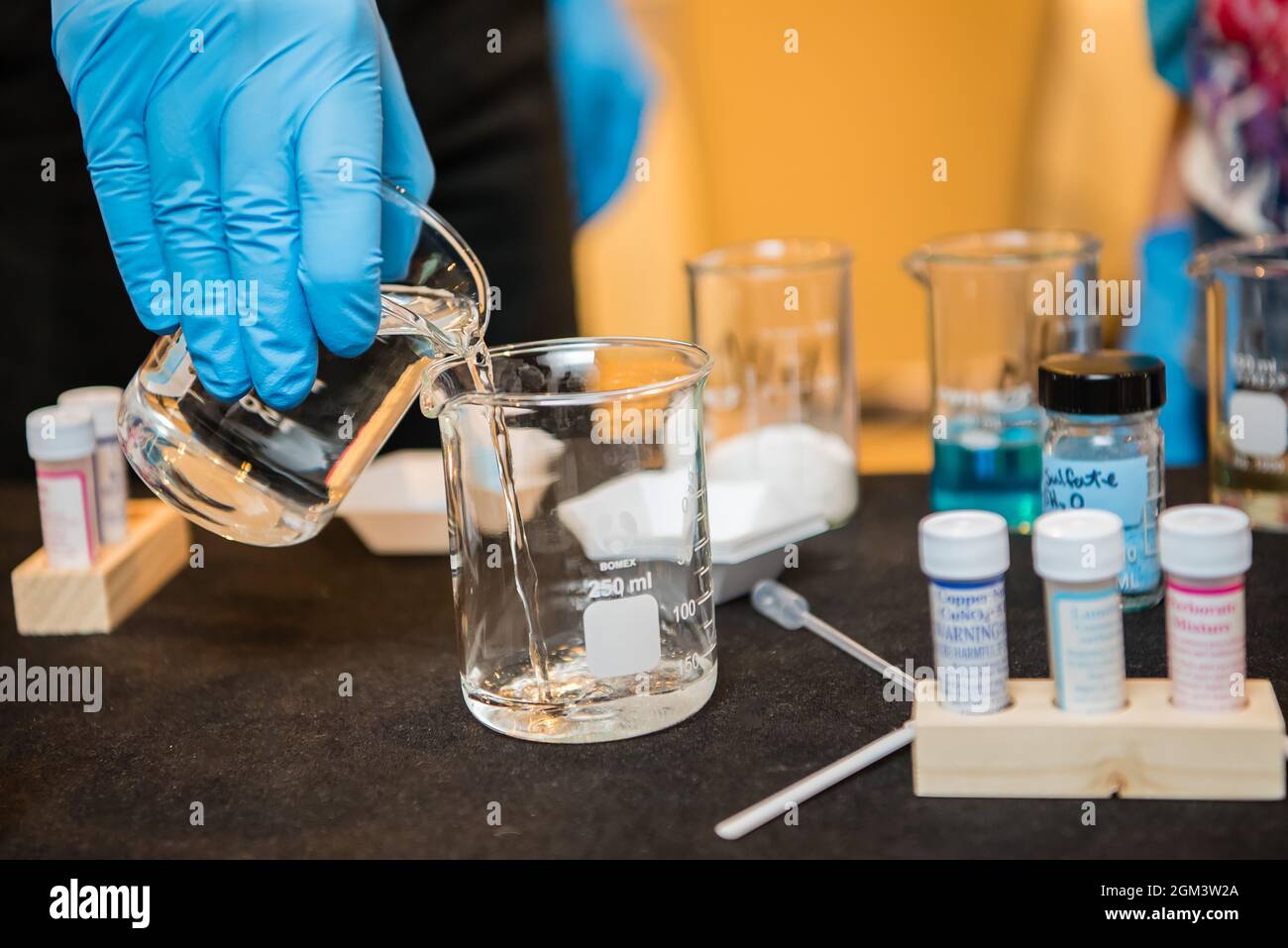 Main gantée en latex verser un bécher de liquide pendant une expérience scientifique en laboratoire scolaire. Banque D'Images