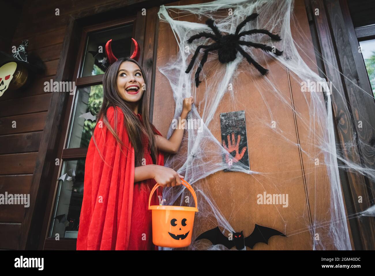 une fille excitée en costume de diable se cognant aux portes avec la décoration d'halloween Banque D'Images