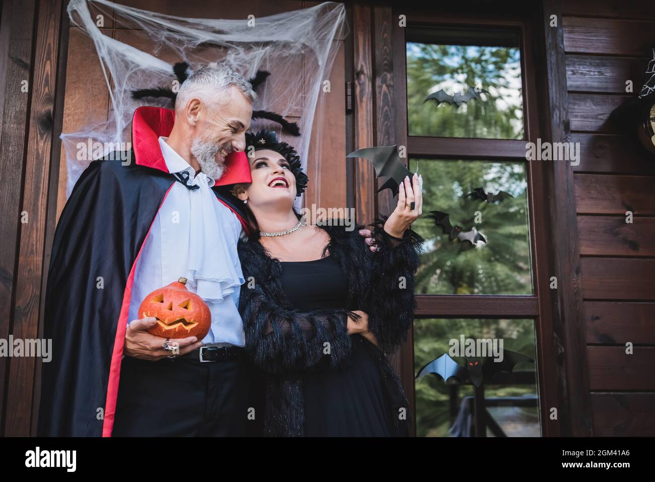homme heureux en costume de vampire tenant la citrouille sculptée et  embrassant la femme sur le porche de la maison avec la décoration  d'halloween Photo Stock - Alamy