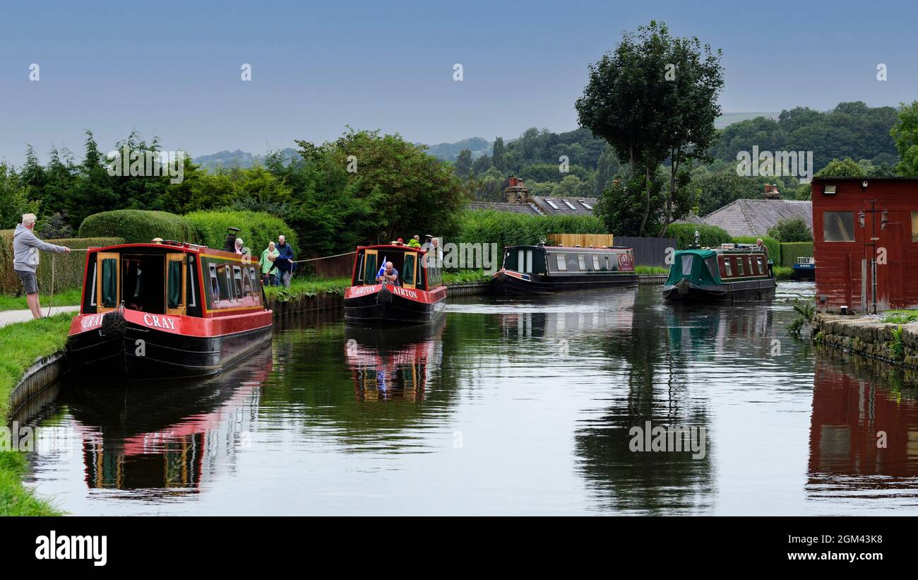 Location de bateaux étroits amarrés et naviguant (personnes se nouant ou se jetant et promeneurs se promenant sur le chemin de halage) - canal pittoresque de Leeds Liverpool, Bingley Angleterre Royaume-Uni. Banque D'Images
