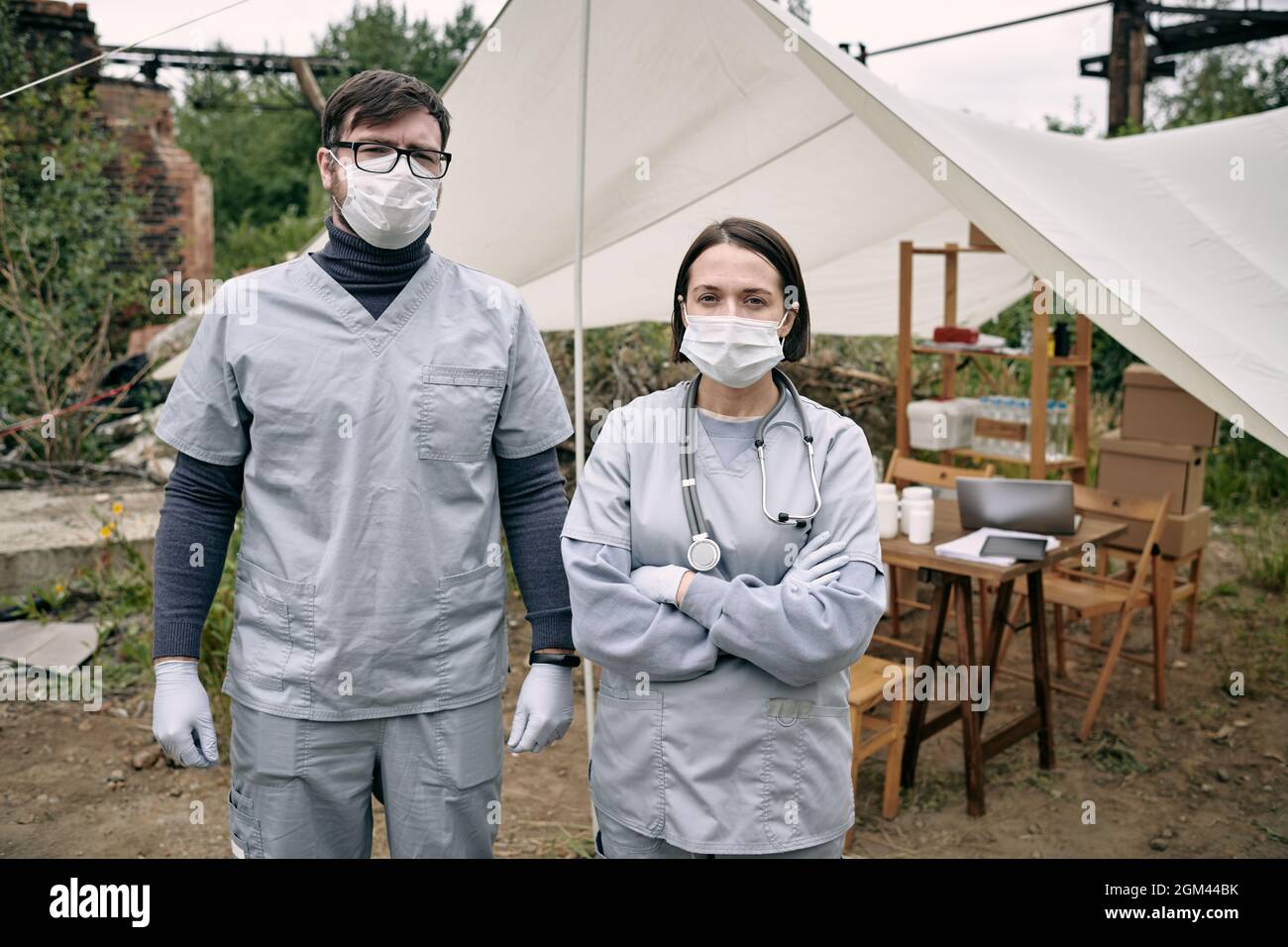 Portrait de jeunes travailleurs médicaux dans des masques et des exfoliants debout contre la tente avec des médicaments dans le camp de réfugiés Banque D'Images