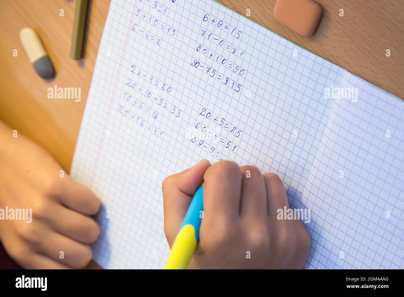 La main d'un élève en gros plan résout des exemples mathématiques dans un bloc-notes. Un écolier effectue une tâche sur le lieu de travail. Le concept de l'éducation, de l'enseignement des connaissances, des compétences et des capacités des enfants. Banque D'Images