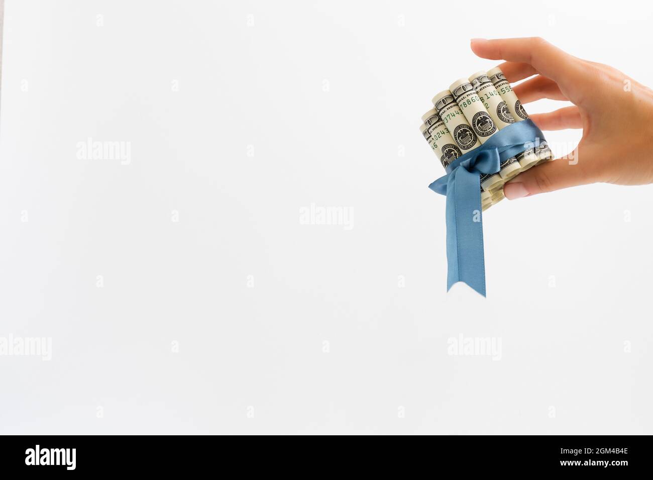 Main féminine tenant des billets roulés de 100 dollars liés avec ruban cadeau bleu. Banque D'Images