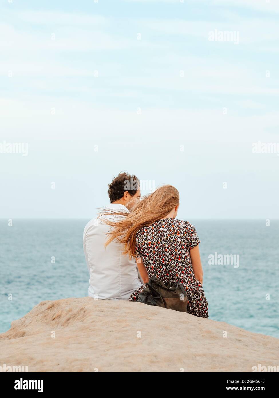 Jeune couple assis sur le rivage de la mer par une journée venteuse Banque D'Images