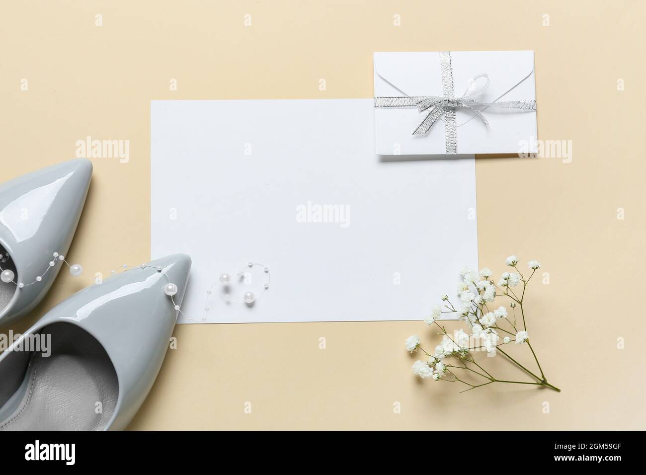 Carte vierge avec enveloppe, fleurs et chaussures sur fond beige Banque D'Images