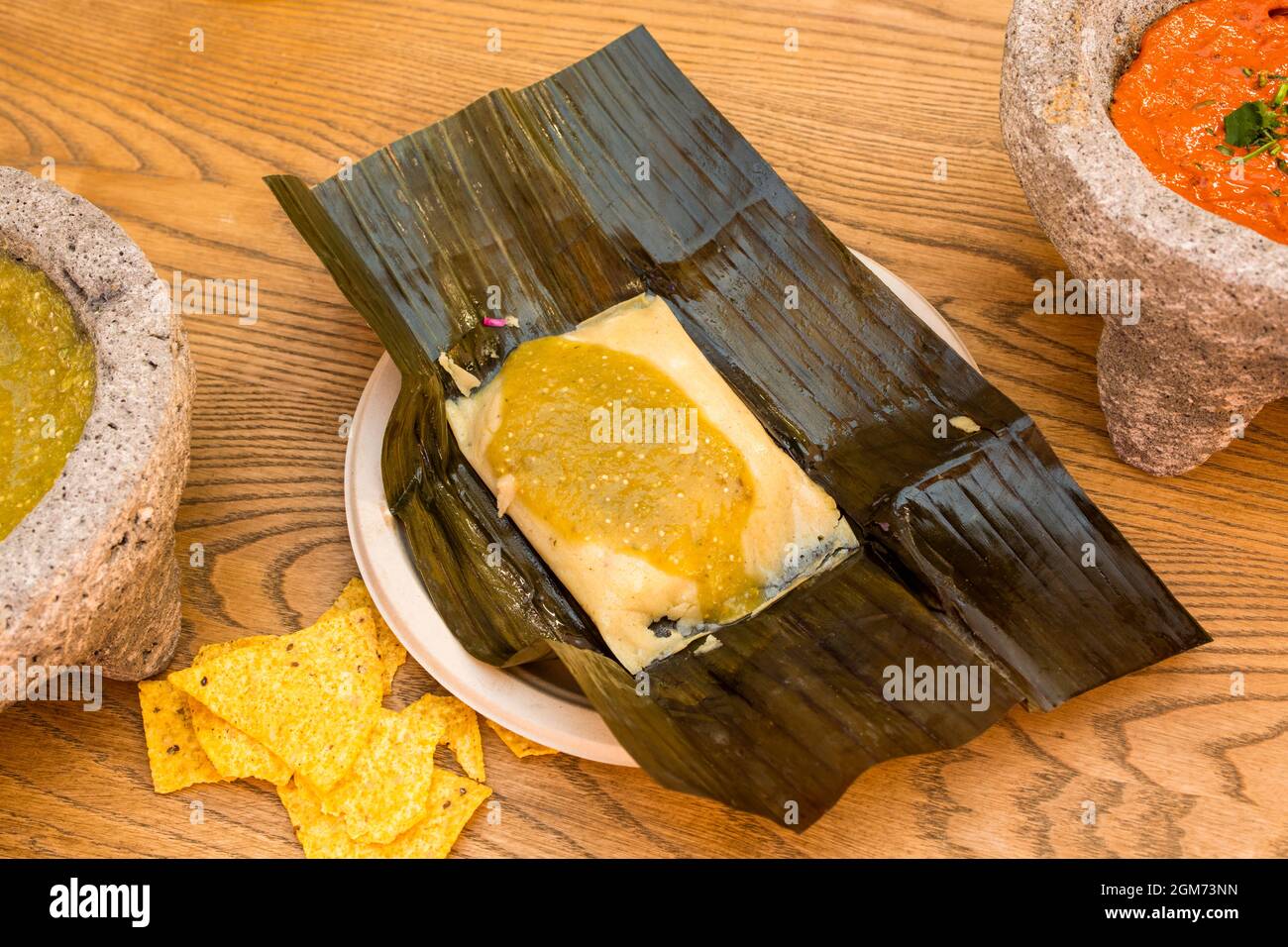 Tamale de poulet mexicaine populaire, sauce verte sur feuille de banane, avec nachos de maïs et molajetes en pierre volcanique Banque D'Images