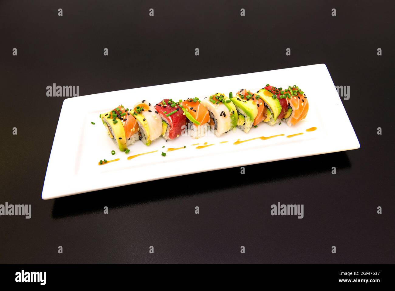 L'uramaki arc-en-ciel avec de l'avocat mûr, du saumon mariné, du thon rouge, de la ciboulette et du poisson-beurre avec de la sauce épicée au soja Banque D'Images