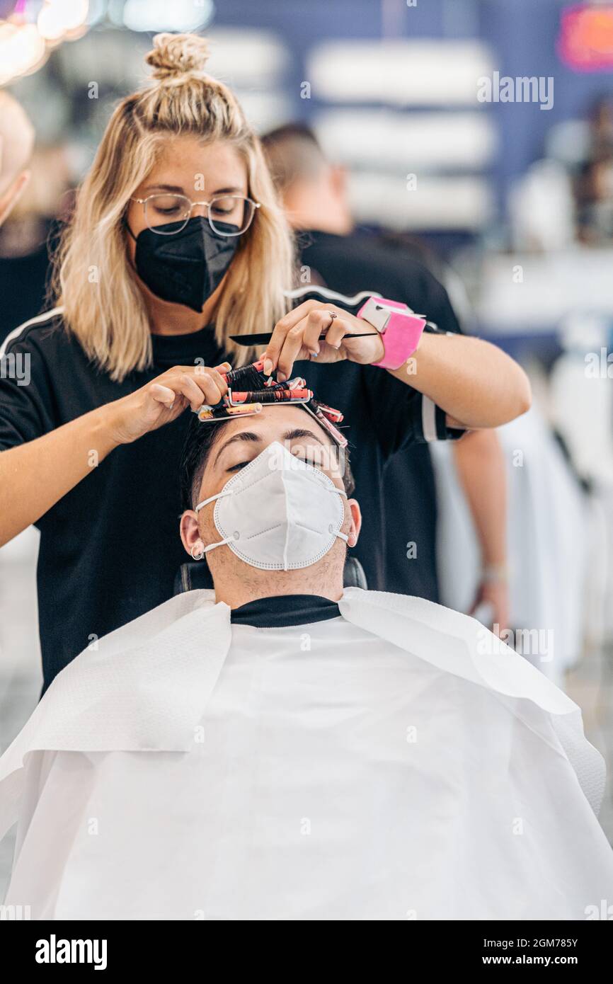 Photo verticale d'un coiffeur en ajustant les boucles des cheveux d'un homme avec masque Banque D'Images