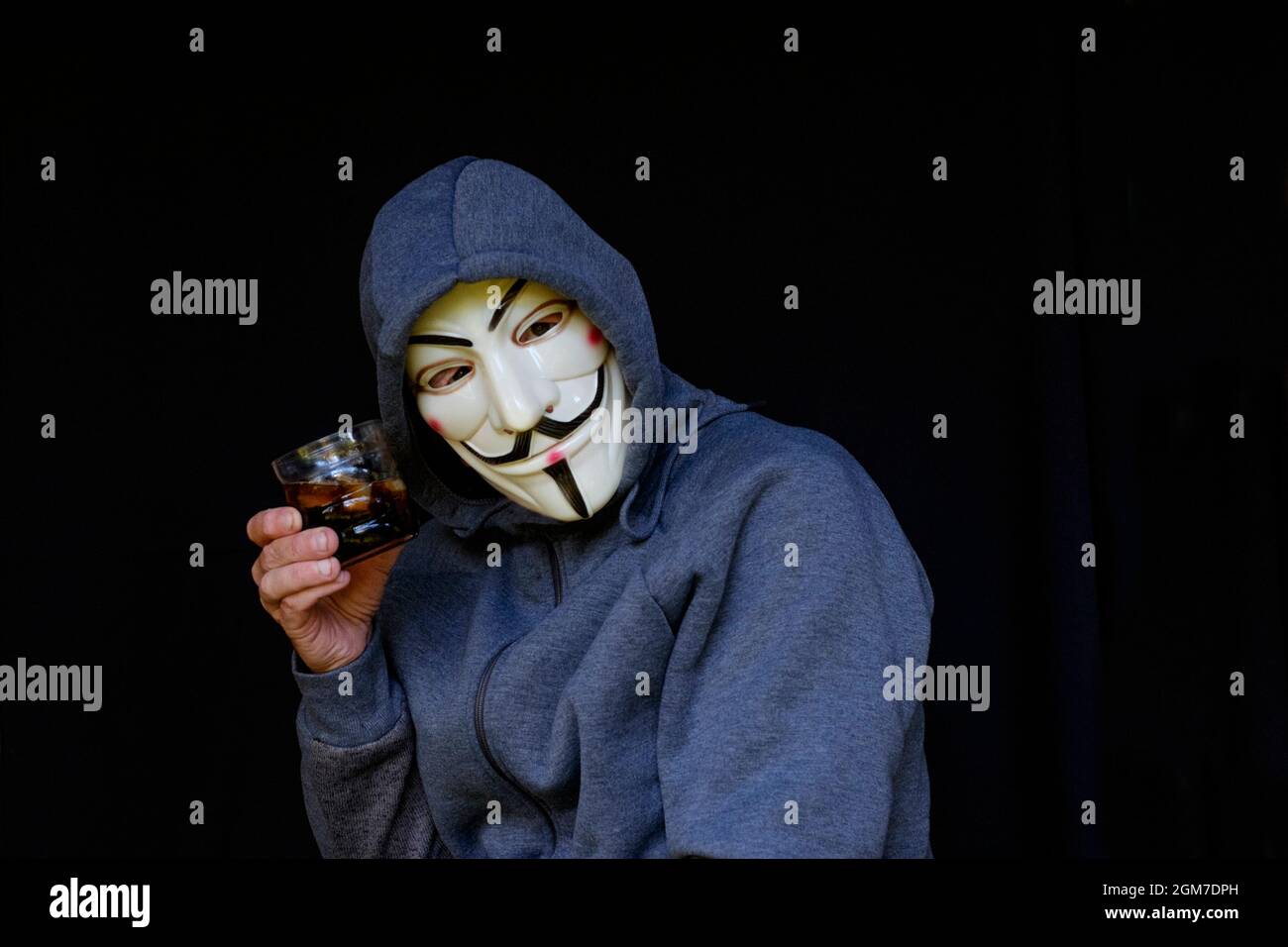 anti vaccin théoricien de conspiration masculin portant le hoodie et v pour le masque vendetta toasts avec le verre d'alcool Banque D'Images
