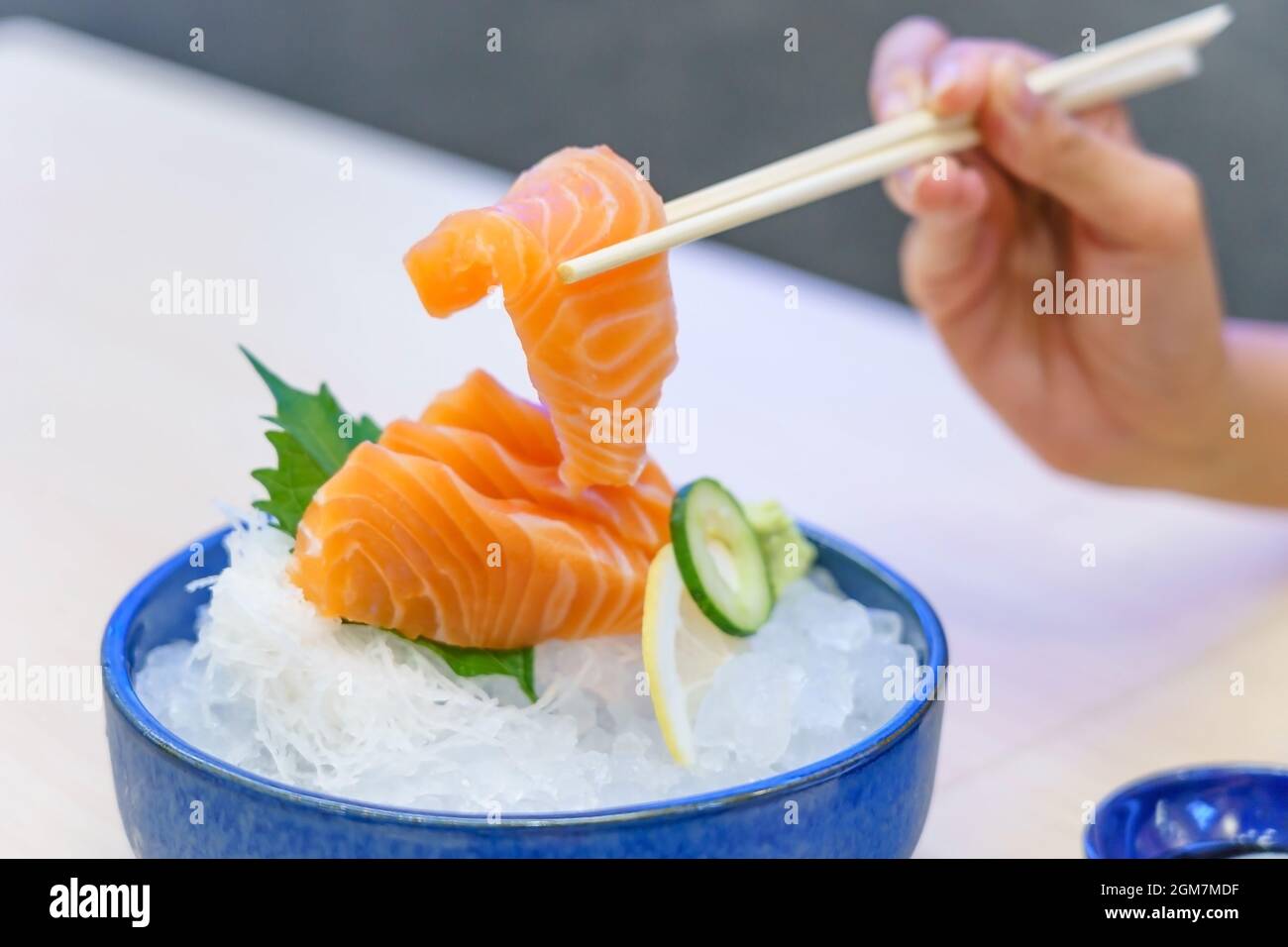 Main tenant le saumon sashimi avec des baguettes - saumon frais cru coupé en tranches sur glace avec wasabi, style japonais. Banque D'Images