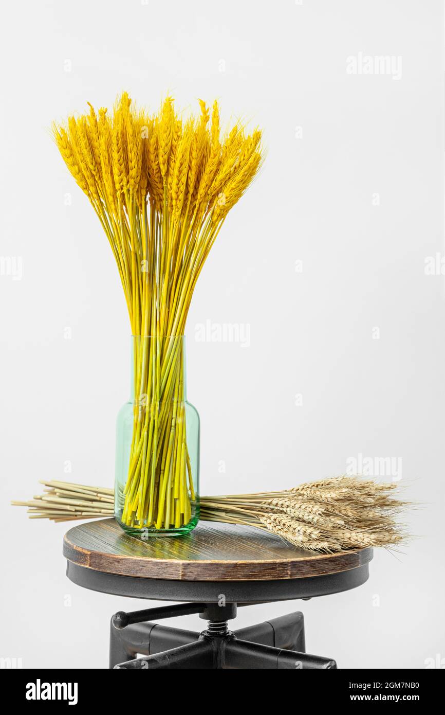 Vase en verre vert rempli de blé jaune et de blé en vrac sur tabouret de style industriel Banque D'Images