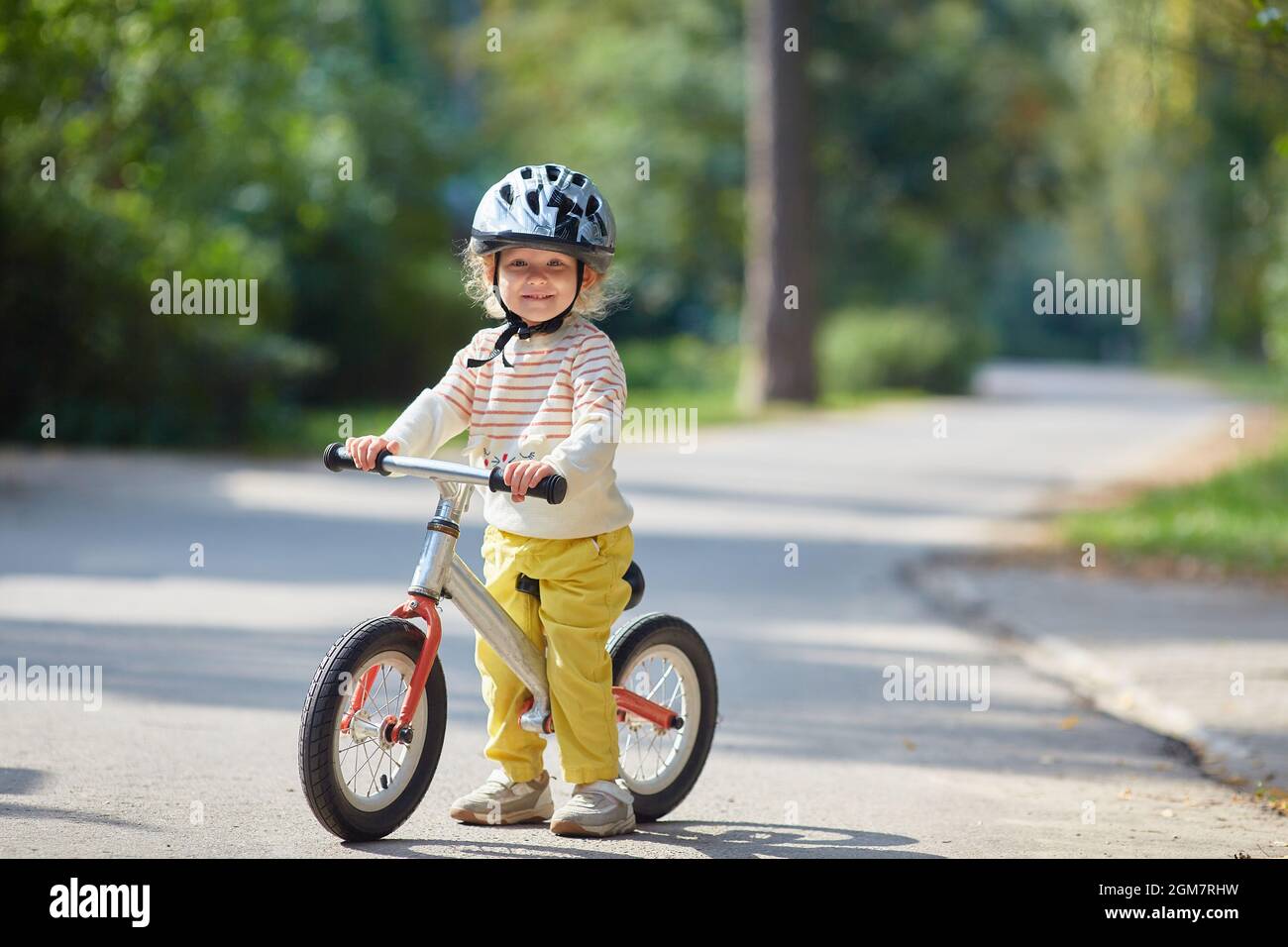 enfant satisfait sur un vélo d'équilibre dans un casque. Un jour d'été ensoleillé. Copier l'espace. Banque D'Images