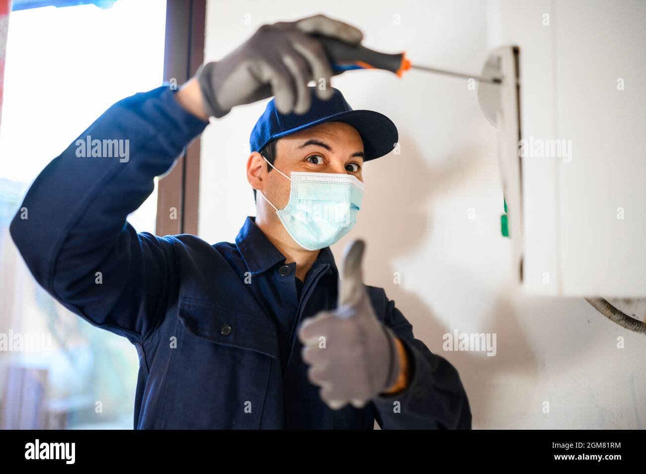 Technicien souriant réparant un chauffe-eau portant un masque, concept de coronavirus Banque D'Images