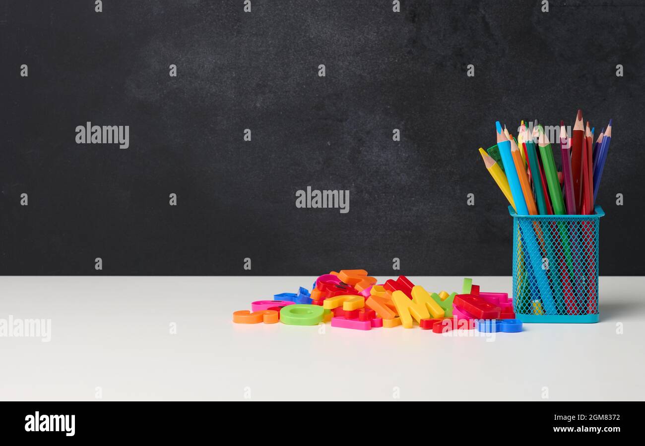 verre métallique avec stylos, crayons et stylos-feutres et ciseaux sur le fond d'un tableau noir vide, table blanche, espace de copie Banque D'Images