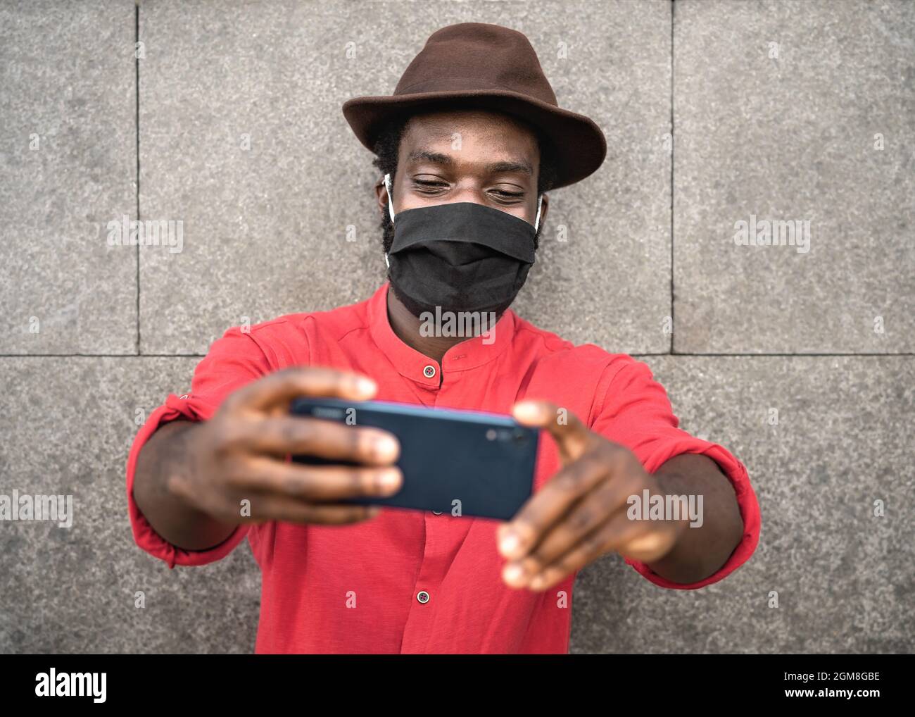 Jeune homme de mode africain prenant le selfie avec un smartphone mobile tout en portant un masque facial pour éviter la propagation du virus corona Banque D'Images