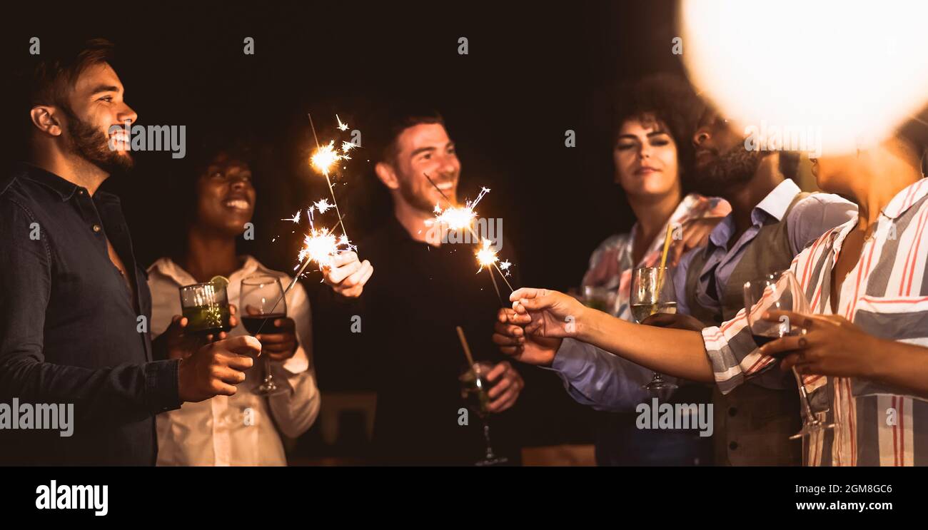 Des jeunes amis heureux s'amuser avec des feux d'artifice de sparklers tout en buvant des cocktails sur la maison patio partie - les jeunes gens style de vie et de vacances concept Banque D'Images