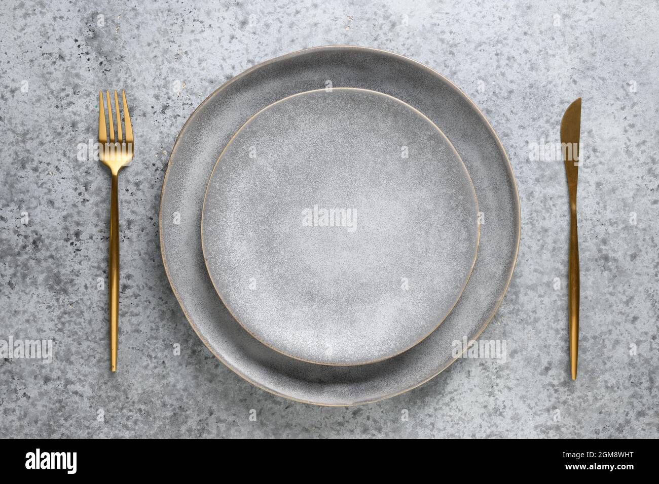 Table vide élégante avec assiette grise vide et couverts dorés comme maquette sur fond de pierre grise. Vue de dessus. Banque D'Images