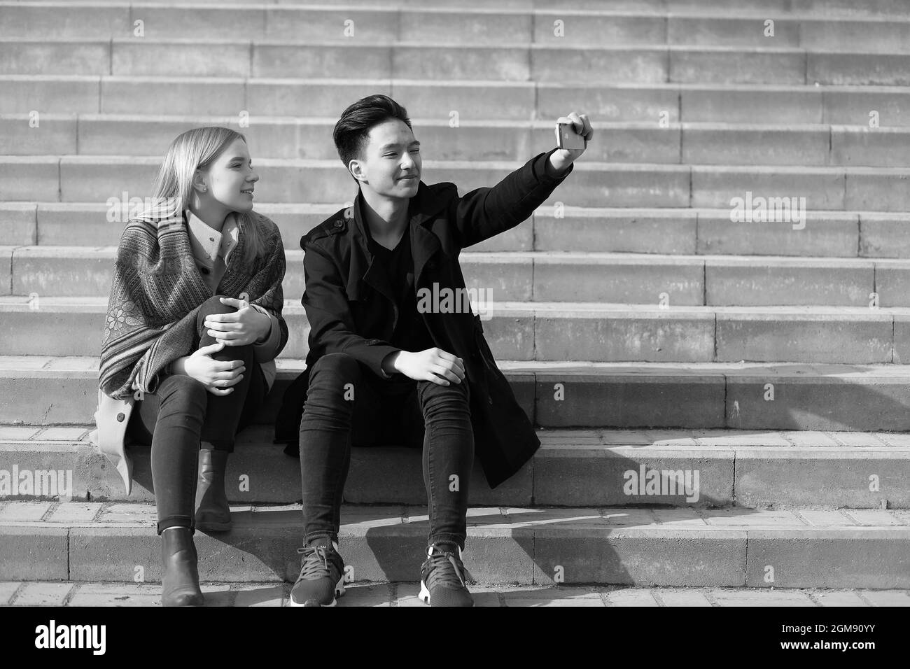 Une paire de jeunes se sont rencontrés dans le parc. Les amoureux sont assis sur un banc dans le parc de la ville. Une asiatique garçon et une fille blanche sont assis sur un banc de parc. Banque D'Images