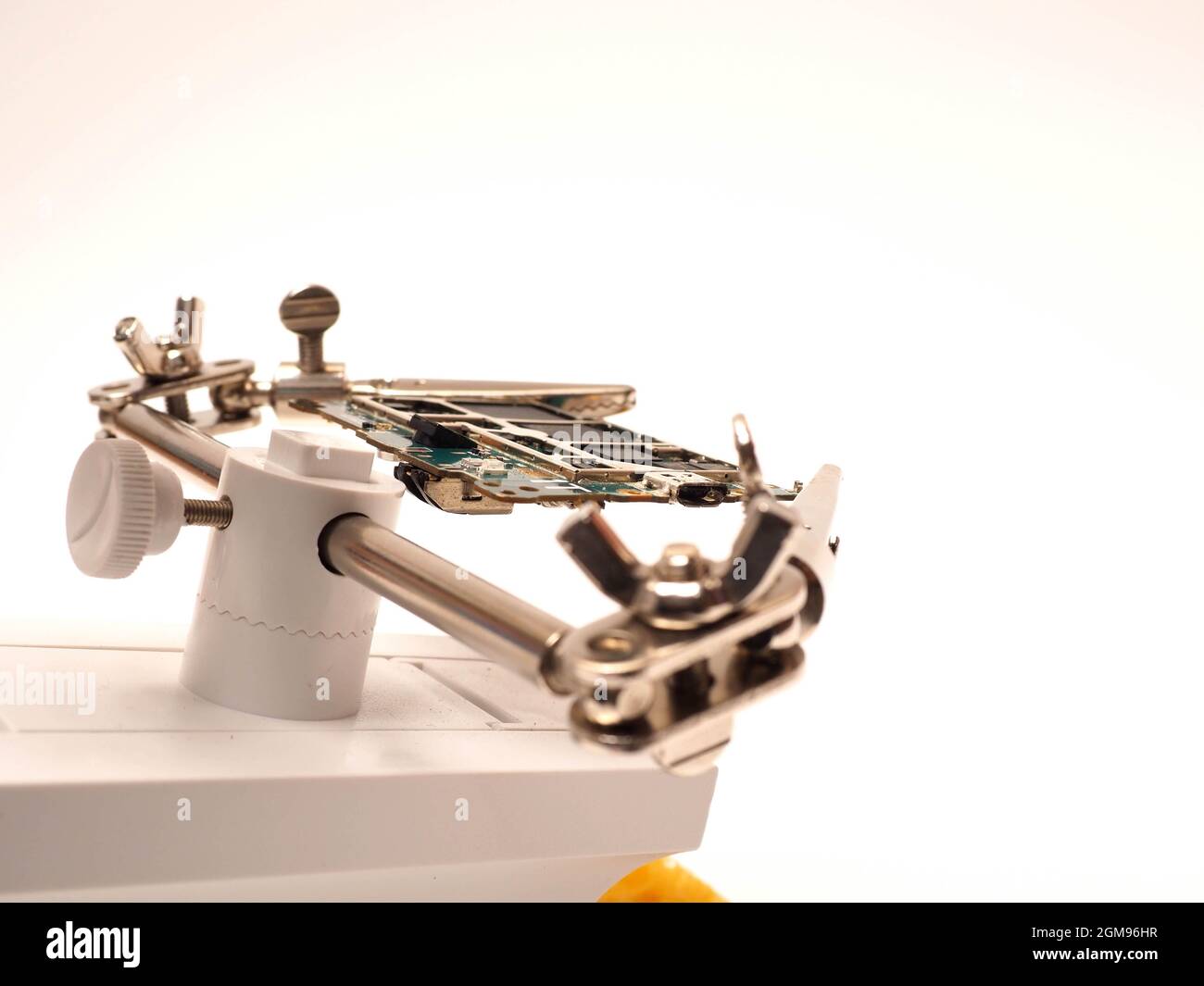 Gros plan d'une carte de circuit imprimé (PCB) reposant sur un support de réparation blanc avec loupe pour mieux examiner les petites pièces. Prenez des photos sur un isolat blanc Banque D'Images