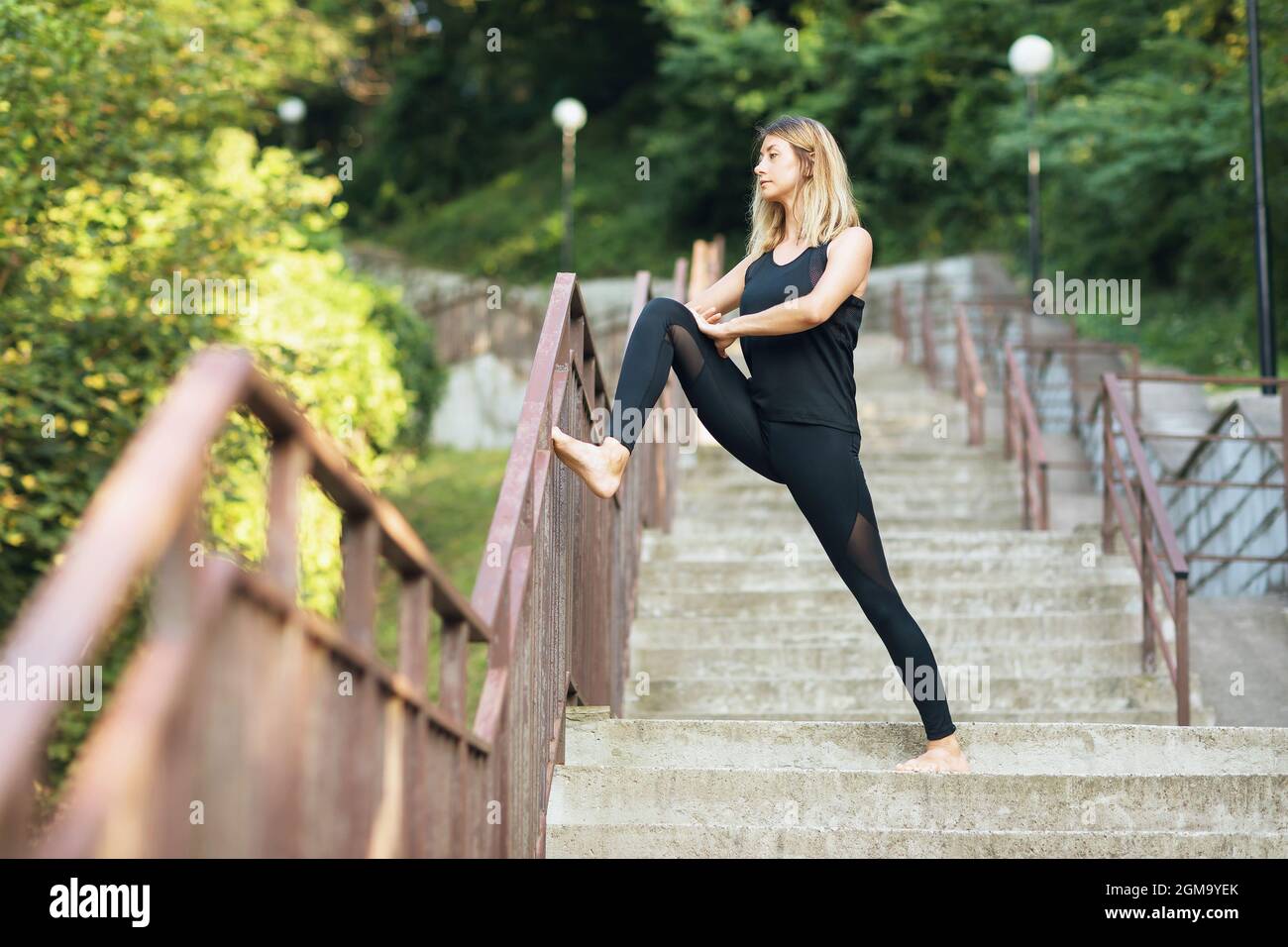 Une femme en vêtements de sport, pratiquant un mode de vie sain, en début de matinée dans le parc, effectue un exercice pour étirer les muscles des jambes Banque D'Images