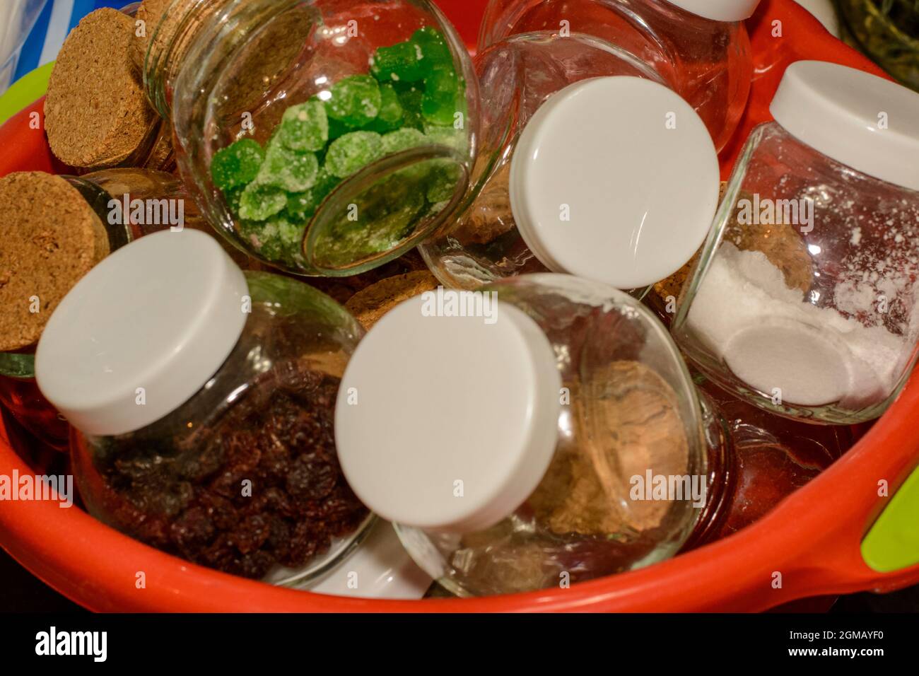Bonbons, nourriture et épices dans de petits pots en verre dans un bol en plastique rouge. Intérieur d'une cuisine résidentielle. Banque D'Images