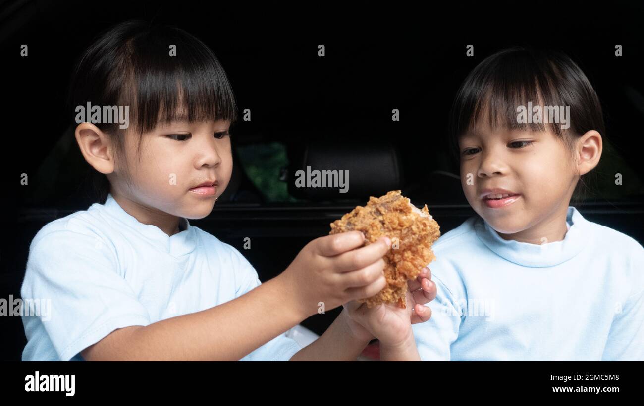 Deux filles sœurs qui ont fait une pause lors d'un voyage en famille et manger du poulet frit dans le coffre de la voiture sur le parc. Service de livraison et distance sociale de Banque D'Images