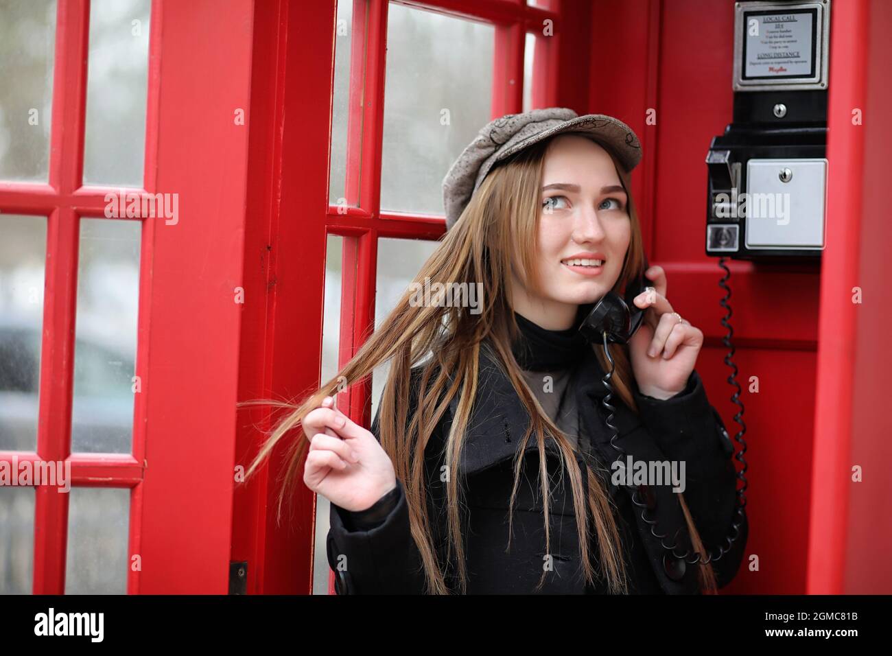 Belle jeune fille dans une cabine téléphonique. La jeune fille parle au  téléphone de la cabine téléphonique. Cabine téléphonique anglaise dans la  rue et une femme qui parle o Photo Stock -