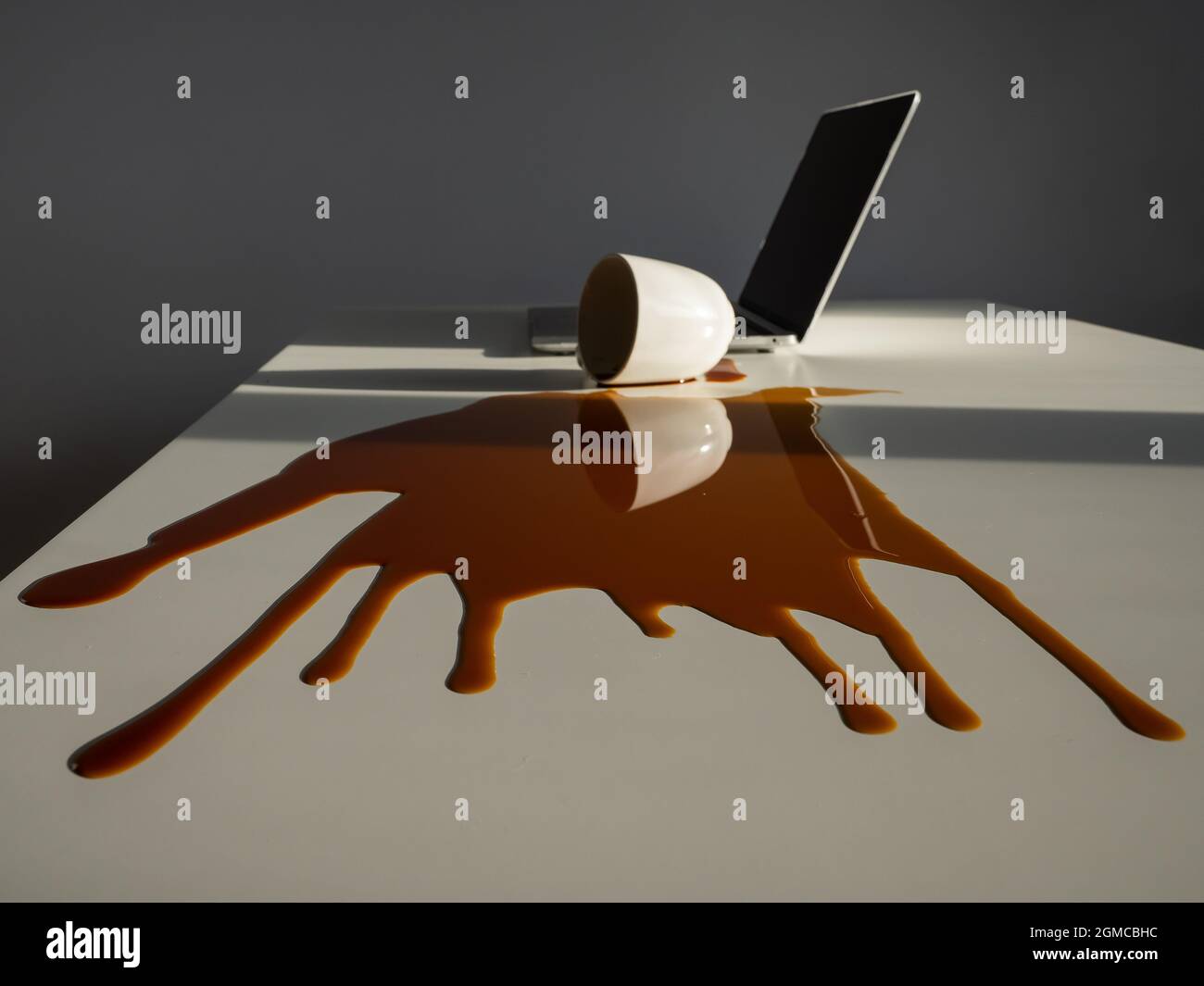 Une tasse de café noir a été renversé sur un ordinateur portable, sur un bureau blanc. Banque D'Images Une tasse de café noir a été renversé sur un ordinateur portable, sur un bureau blanc. Banque D'Images