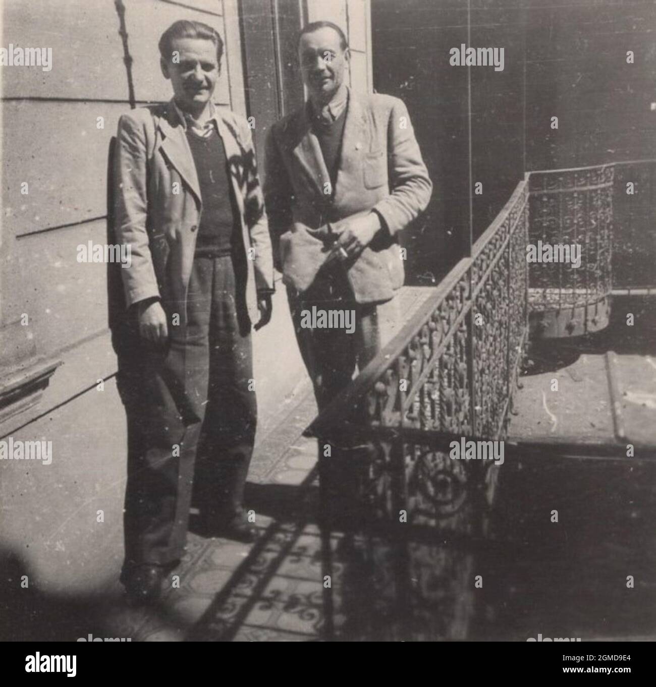 photographie vintage originale des années 1940. deux messieurs sont debout sur le balcon. Ils fument, chuchotent. Photo typique de j'ai quelques ragots juteux pour toi. Avez-vous entendu les (derniers) commérages ? n'est-ce pas ? source : photo originale / homme vintage fumant une cigarette Banque D'Images