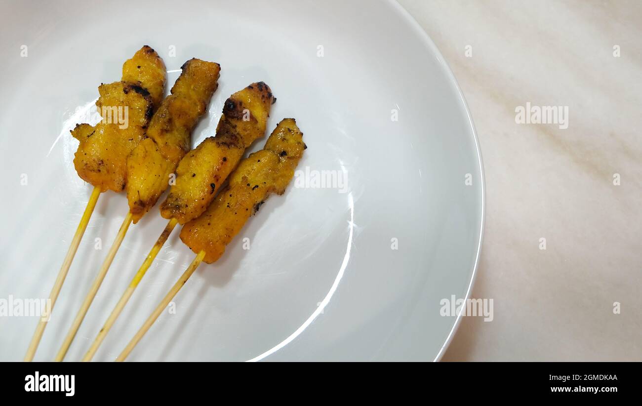 Quatre satay de poulet servi sur une assiette ronde blanche, placée sur une surface en marbre. Banque D'Images