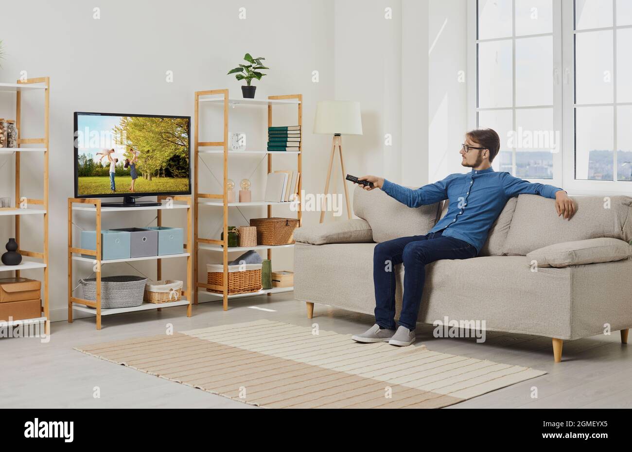 Un jeune homme se détendant sur un canapé dans le salon et regardant un film sur grand écran de télévision moderne Banque D'Images