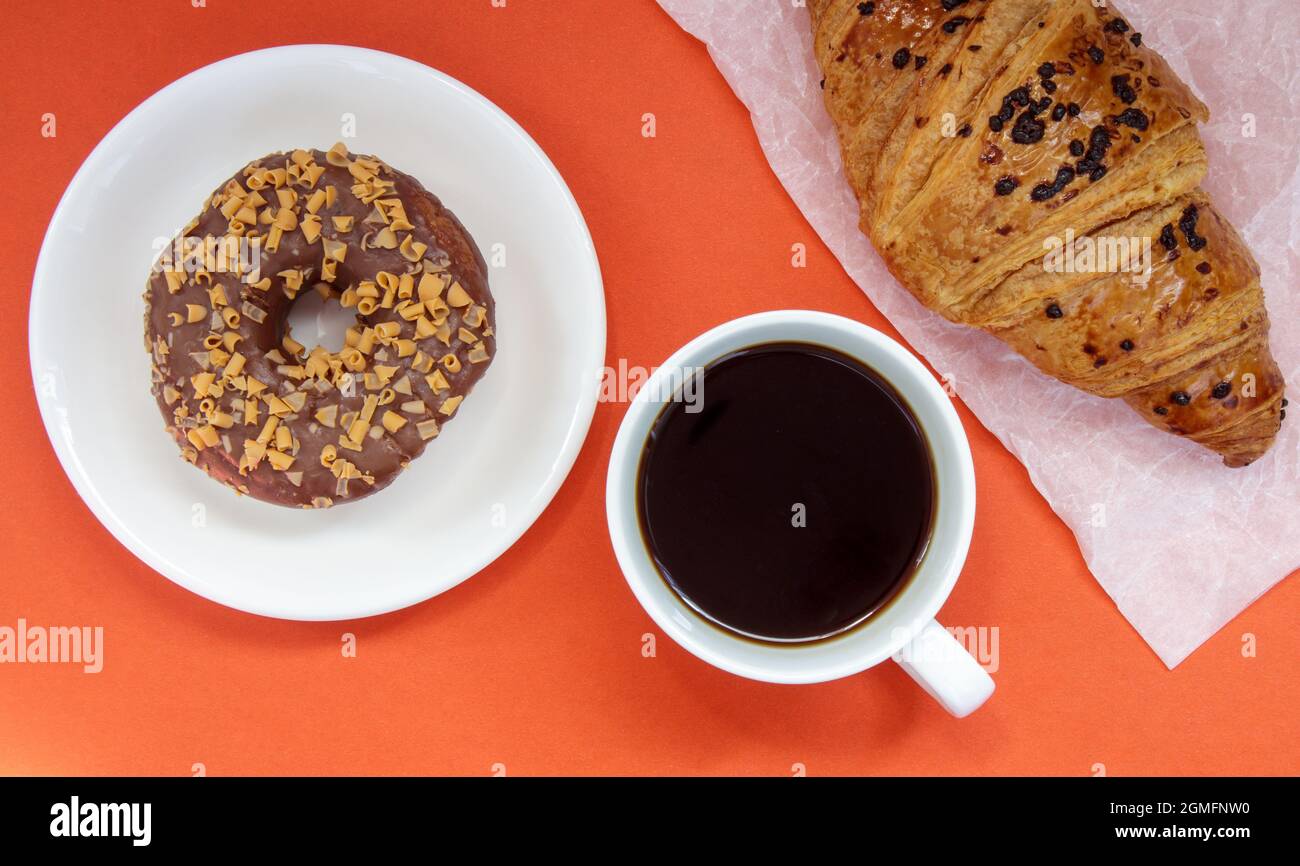 Un beignet au chocolat, un croissant et un café américain noir sans lait dans une tasse blanche sur fond clair.Vue de dessus, plan d'appartement.Fraîchement préparé ou Banque D'Images