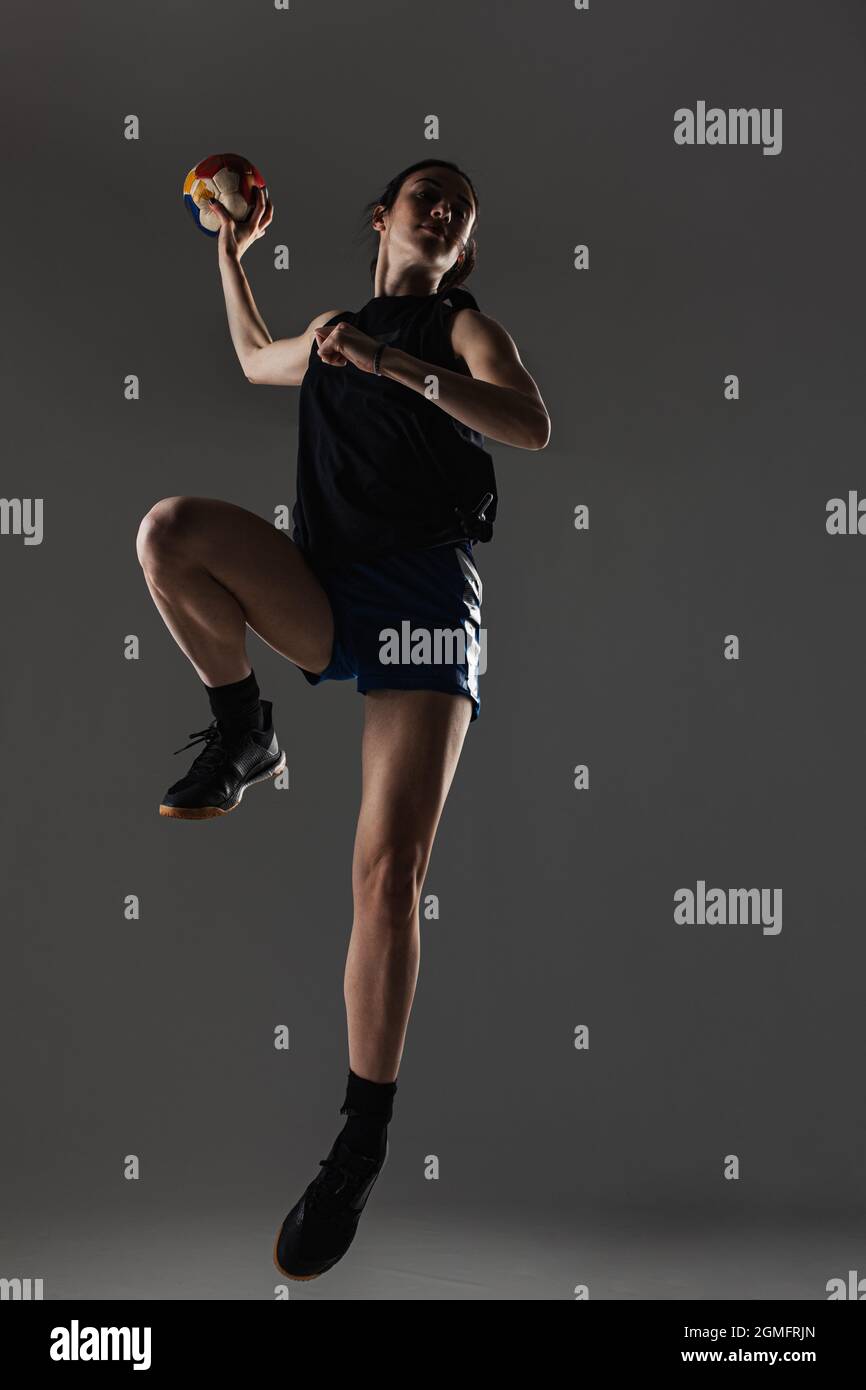 Joueur de handball posé sur fond gris. Fille sautant avec le ballon. Banque D'Images