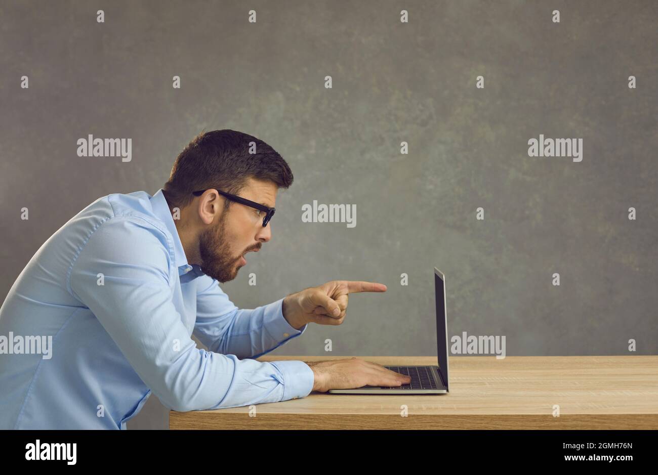 Vue latérale d'un homme choqué assis sur un bureau et regardant un ordinateur portable pointant vers l'écran Banque D'Images