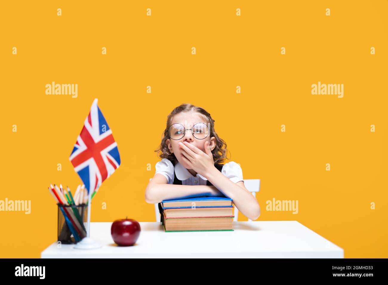 Ennuyeux école caucasienne s'assoit à la réception avec pile de livres. Cours d'anglais. Drapeau de la Grande-Bretagne Banque D'Images