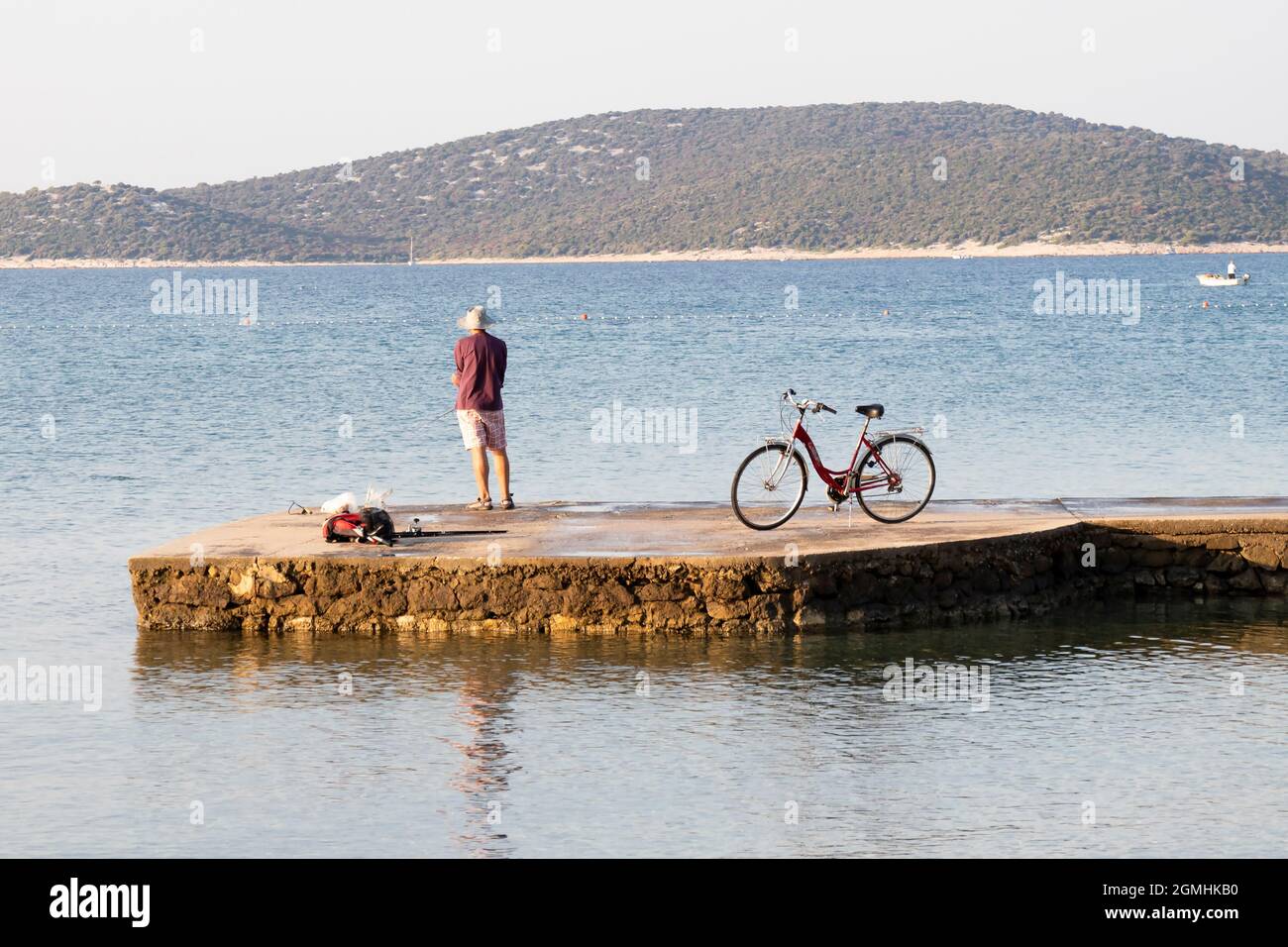Vodice, Croatie - 16 août 2021 : jeune homme debout seul sur un quai maritime et pêchant avec son vélo stationné à côté de lui Banque D'Images