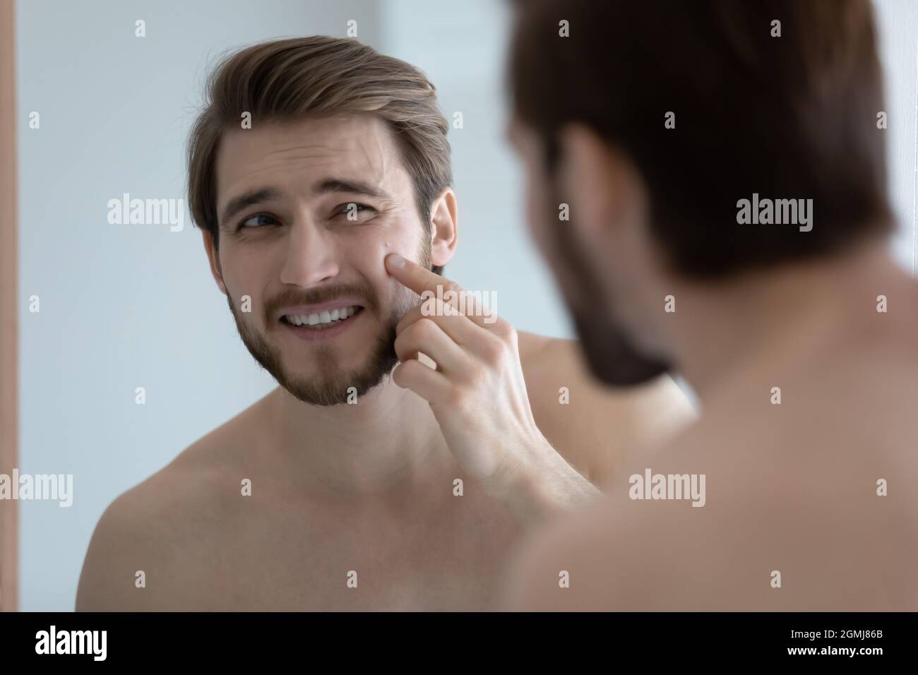 Homme regardant dans le miroir face tactile avec bouton sur le pommettes Banque D'Images